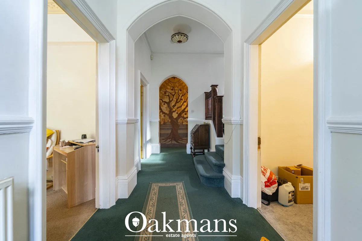 Bright hallway with arched ceiling, white pillars, green carpet, ornate artwork and wooden furniture pieces