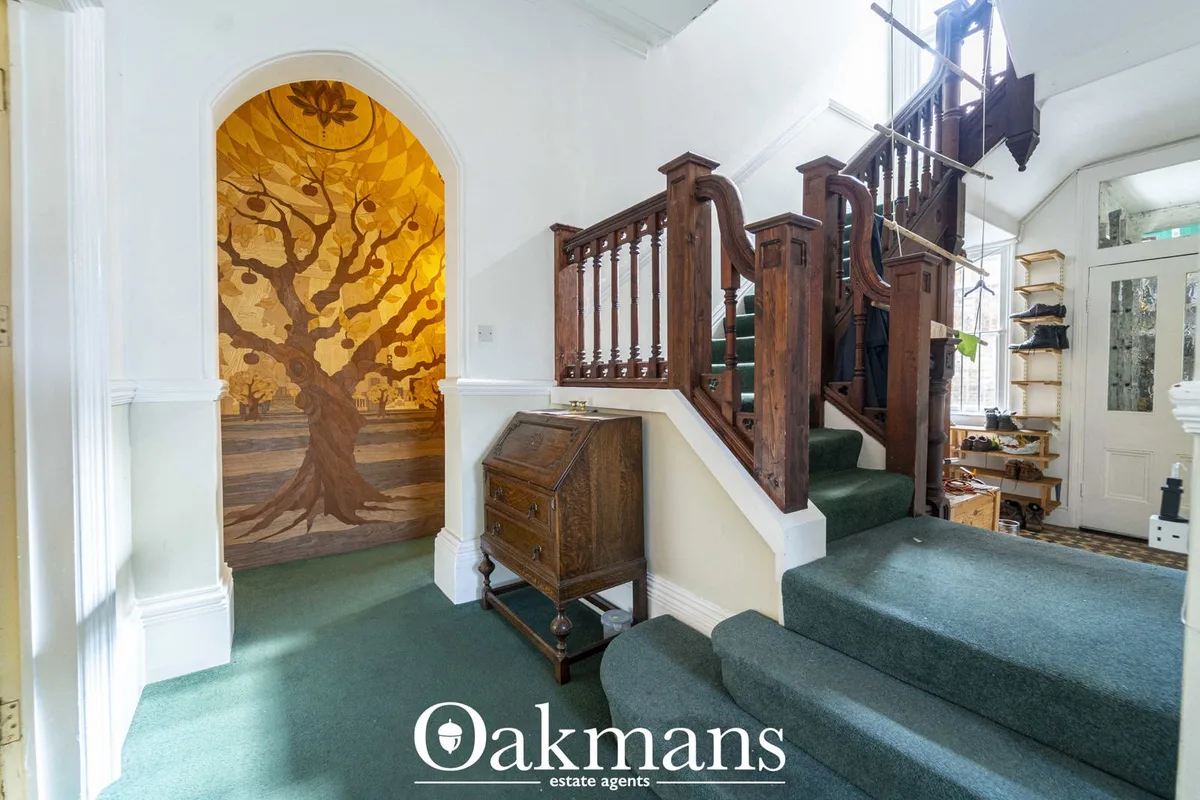 Bright hallway with wooden staircase, arched niche featuring tree mural artwork, antique furniture and green carpet