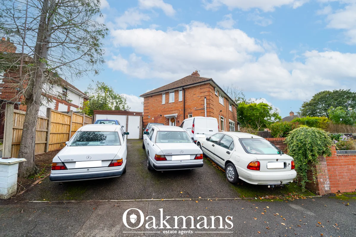 Brick suburban house with driveway showing three white parked cars, wooden fencing, bare tree and blue sky