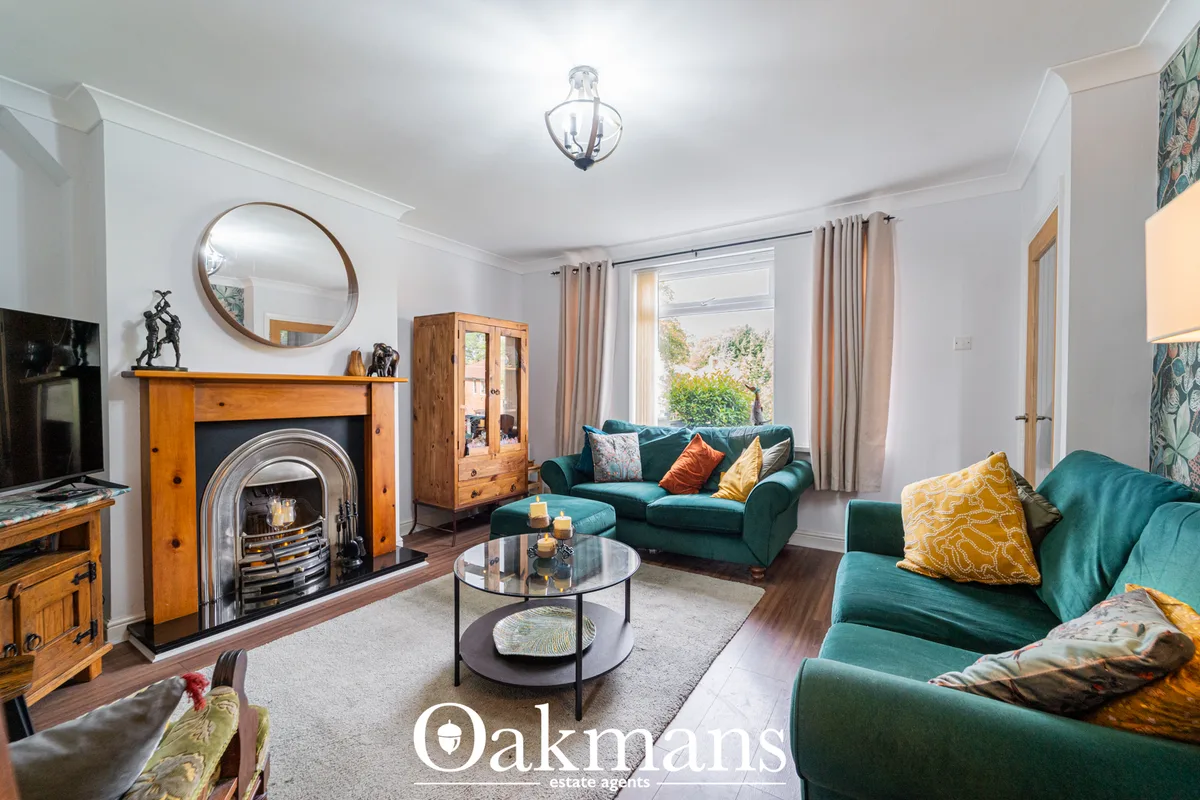 Bright living room with teal velvet sofas, fireplace with wooden surround, round mirror, coffee table, and large windows