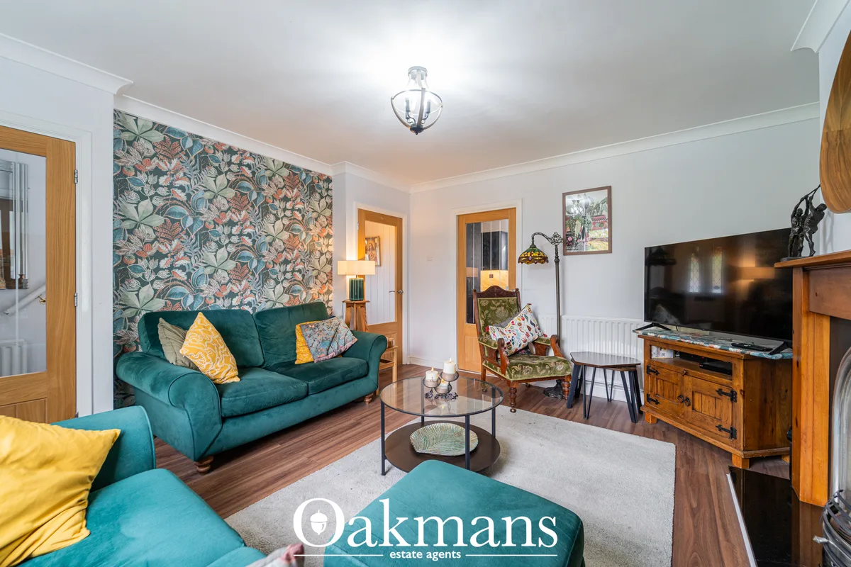 Spacious living room with teal sofa, floral feature wall, wooden furniture, flat-screen TV, patterned armchair and doorw