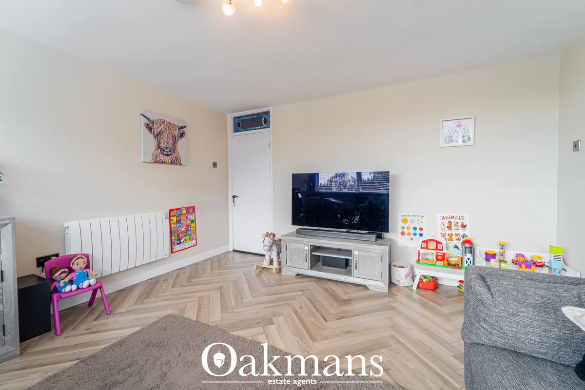 Bright living room with herringbone wood flooring, wall-mounted TV, white radiator, cream walls, children's toys and fur