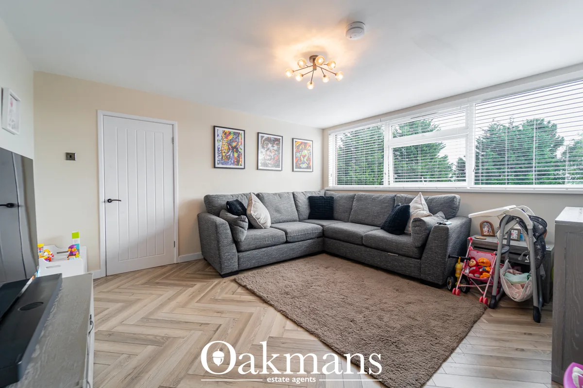 Spacious living room with grey corner sofa, herringbone wood flooring, beige walls, large windows with blinds and childr