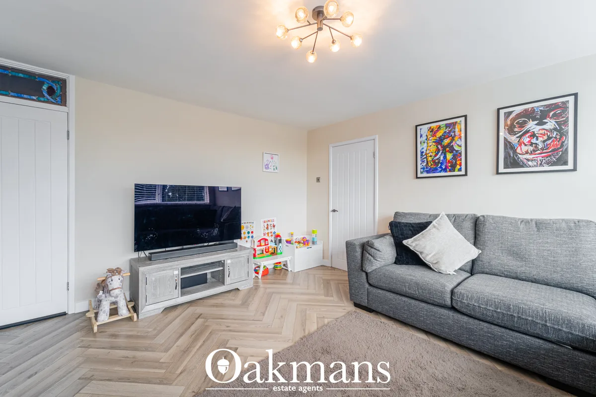 Spacious living room with grey sofa, wall-mounted TV on white media unit, herringbone wood flooring, and framed artwork 