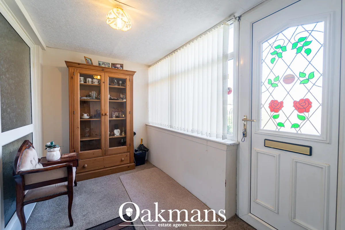 Bright entrance hallway with wooden display cabinet, vertical blinds, glazed door with floral window panel, ceiling ligh