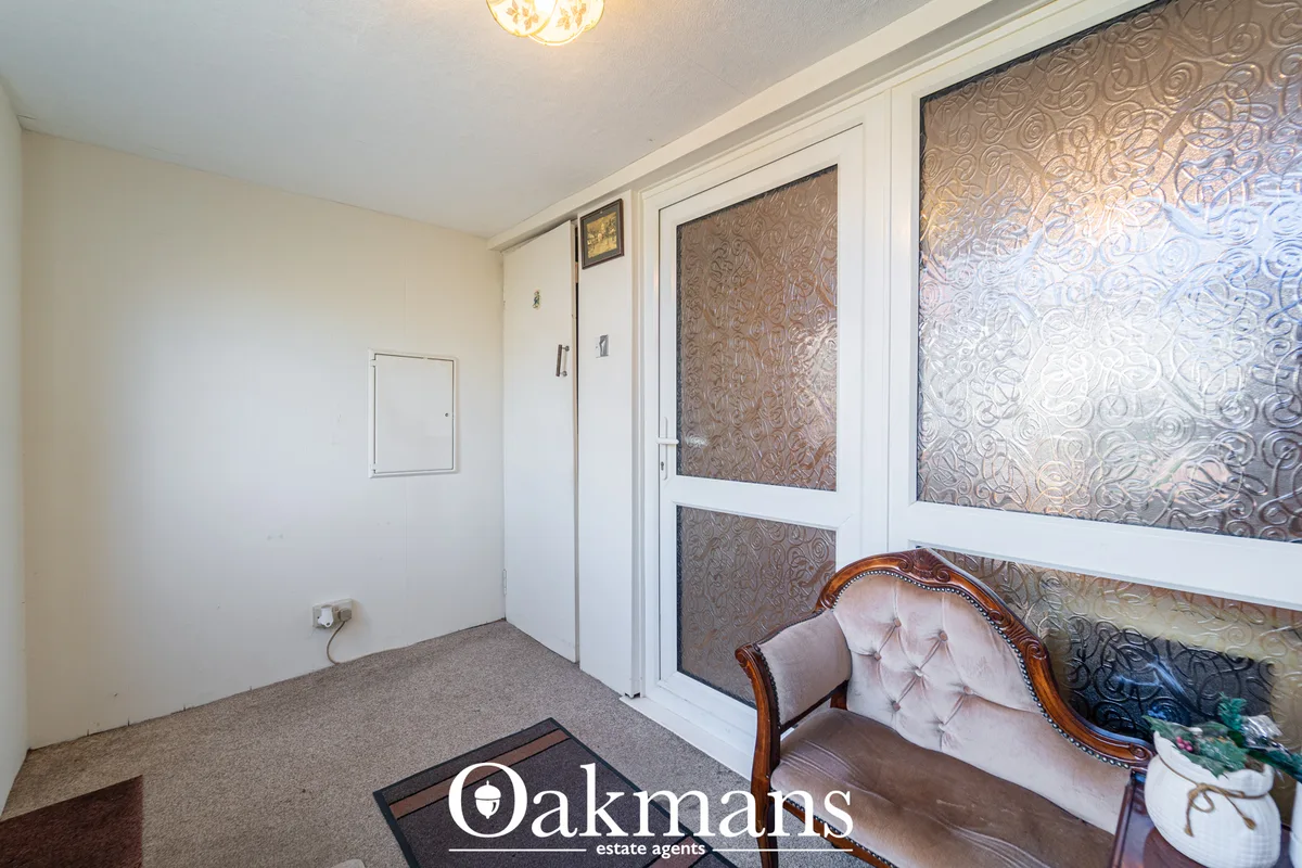Cream and white hallway with fitted wardrobes, patterned door panels, ceiling light, and upholstered chair in corner