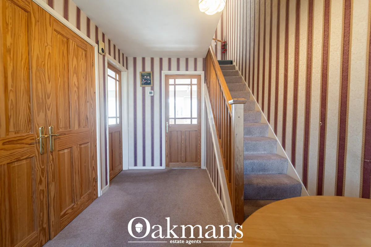 Entrance hallway with wooden doors on left, striped wallpaper, staircase with wooden banister on right, and glass-panell