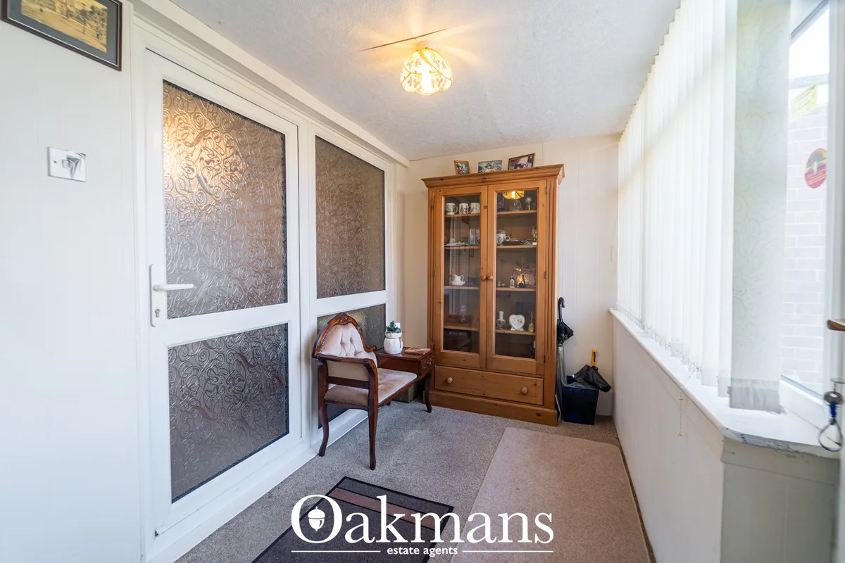 Bright hallway with patterned glass doors, wooden display cabinet, chair, windows, and cream carpet flooring