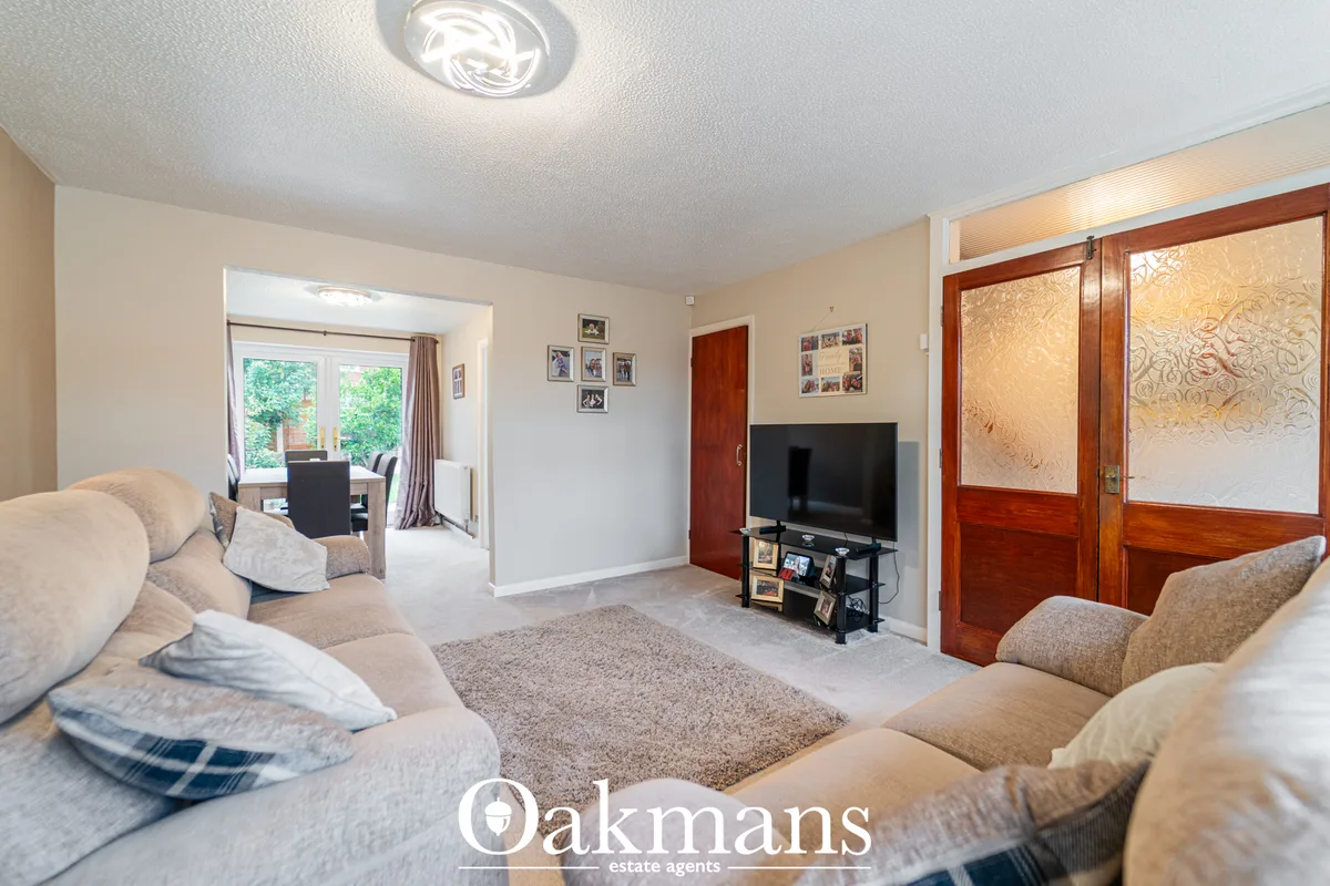 Spacious living room with beige sofas, TV on black stand, grey rug, cream walls, wooden doors, and access to dining area