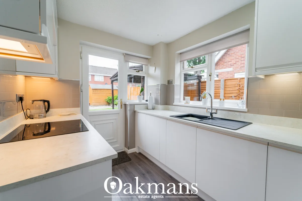 Modern white fitted kitchen with granite worktops, induction hob, sink with mixer tap, and garden views through patio do
