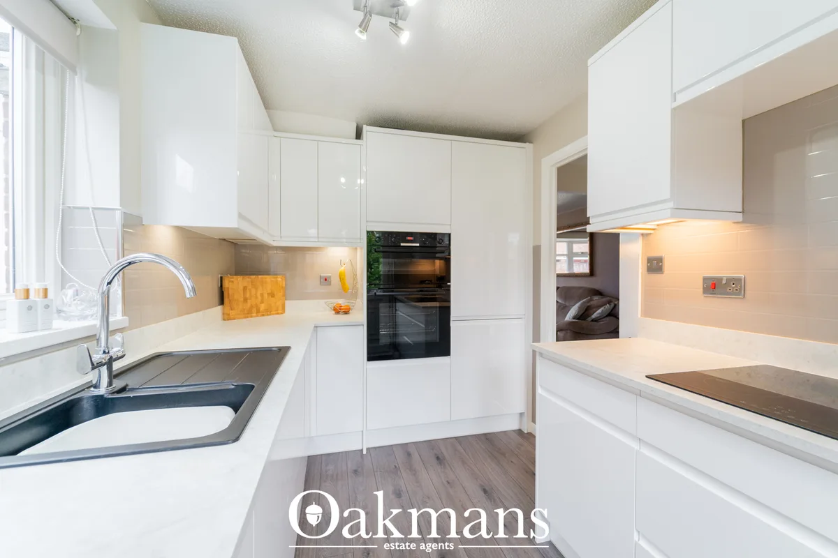 Modern fitted kitchen with white gloss units, cream worktops, integrated black oven, chrome tap and wooden flooring