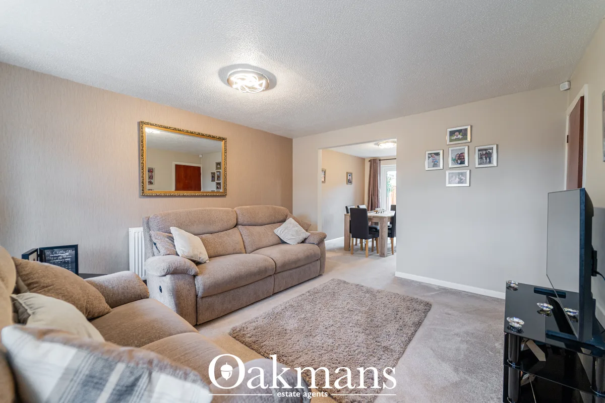 Spacious living room with beige upholstered sofas, grey area rug, framed mirror, ceiling spotlights, and open-plan acces