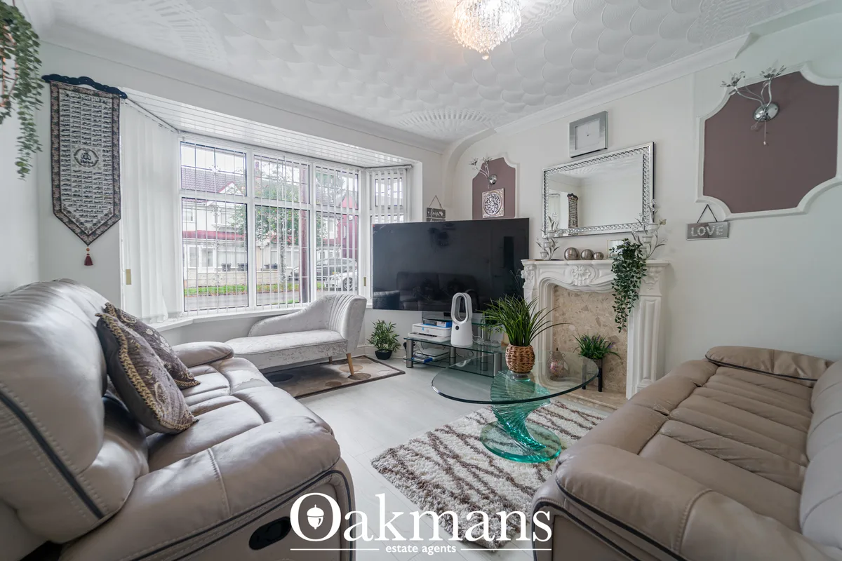 Spacious living room with cream leather sofas, fireplace with ornate surround, large flat-screen TV, patterned rug, indo