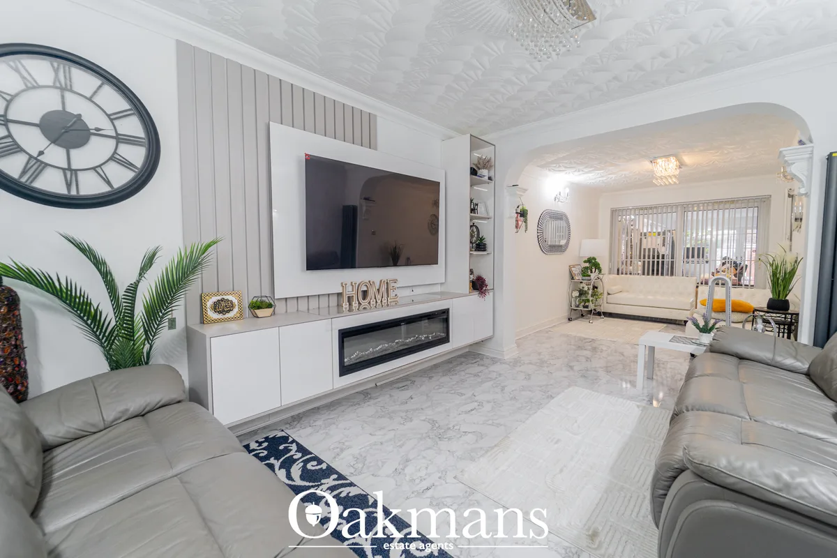 Contemporary living room with grey leather sofas, white feature wall with wall-mounted TV and fireplace, houseplants, de