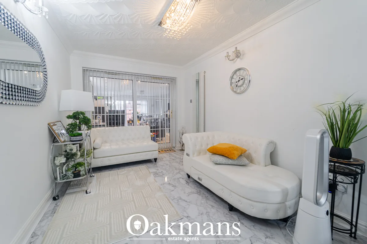 Bright living room with two white upholstered sofas, marble flooring, decorative wall clock, patterned mirror, potted pl