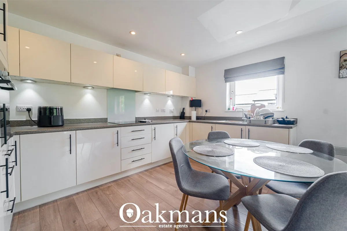 Modern fitted kitchen with cream units, grey worktops, white splashback, breakfast bar and dining table with grey chairs