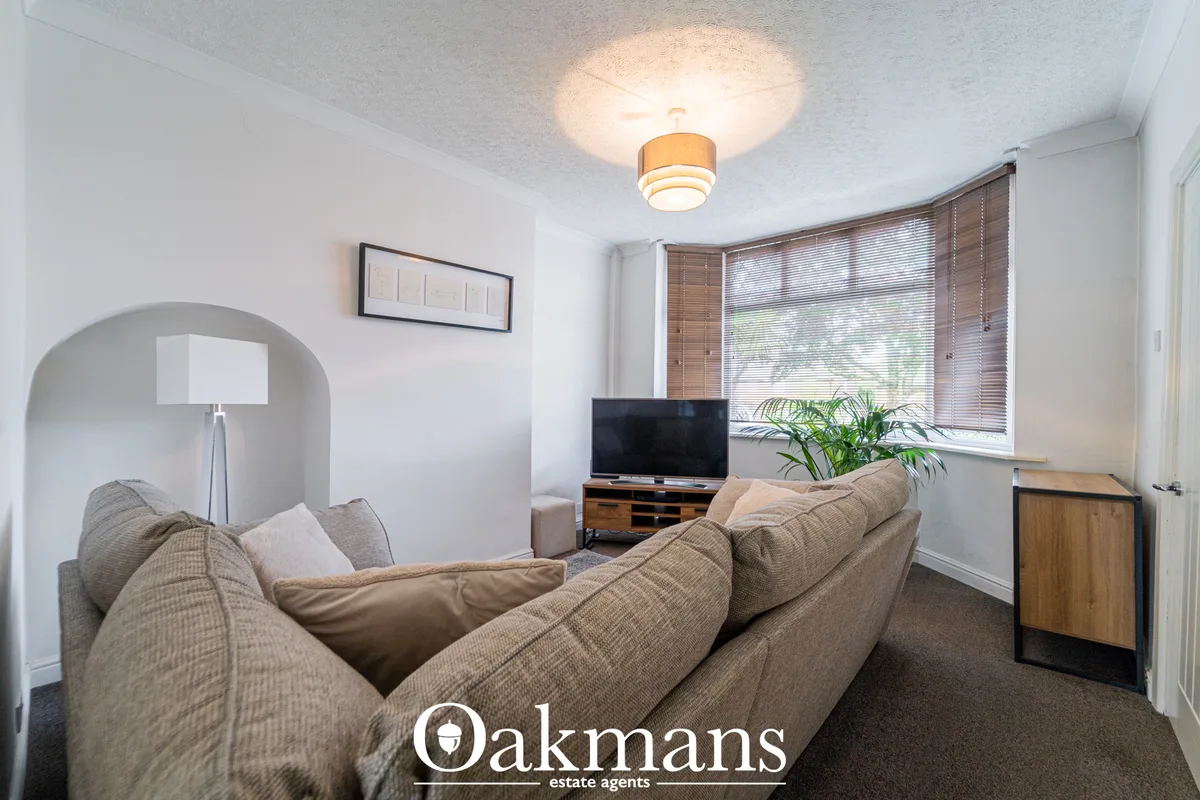 Bright living room with beige upholstered sofa, wooden TV unit, pendant ceiling light, large bay window with wooden blin