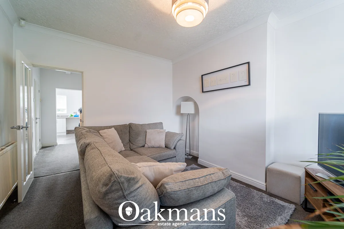 Bright living room with grey upholstered armchair and sofa, neutral walls, ceiling light, wall art, floor lamp and parti
