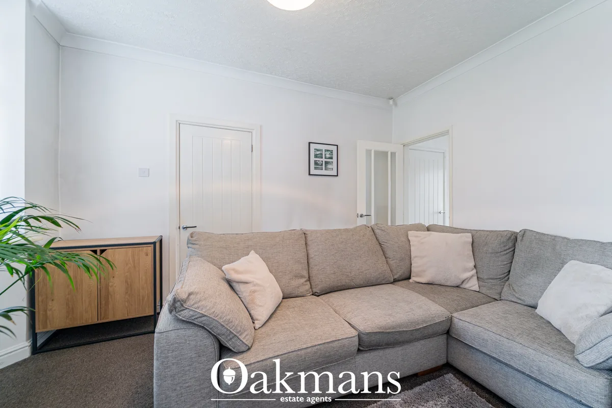 Spacious living room with beige corner sofa, wooden sideboard, potted plant, white walls and doors, recessed lighting