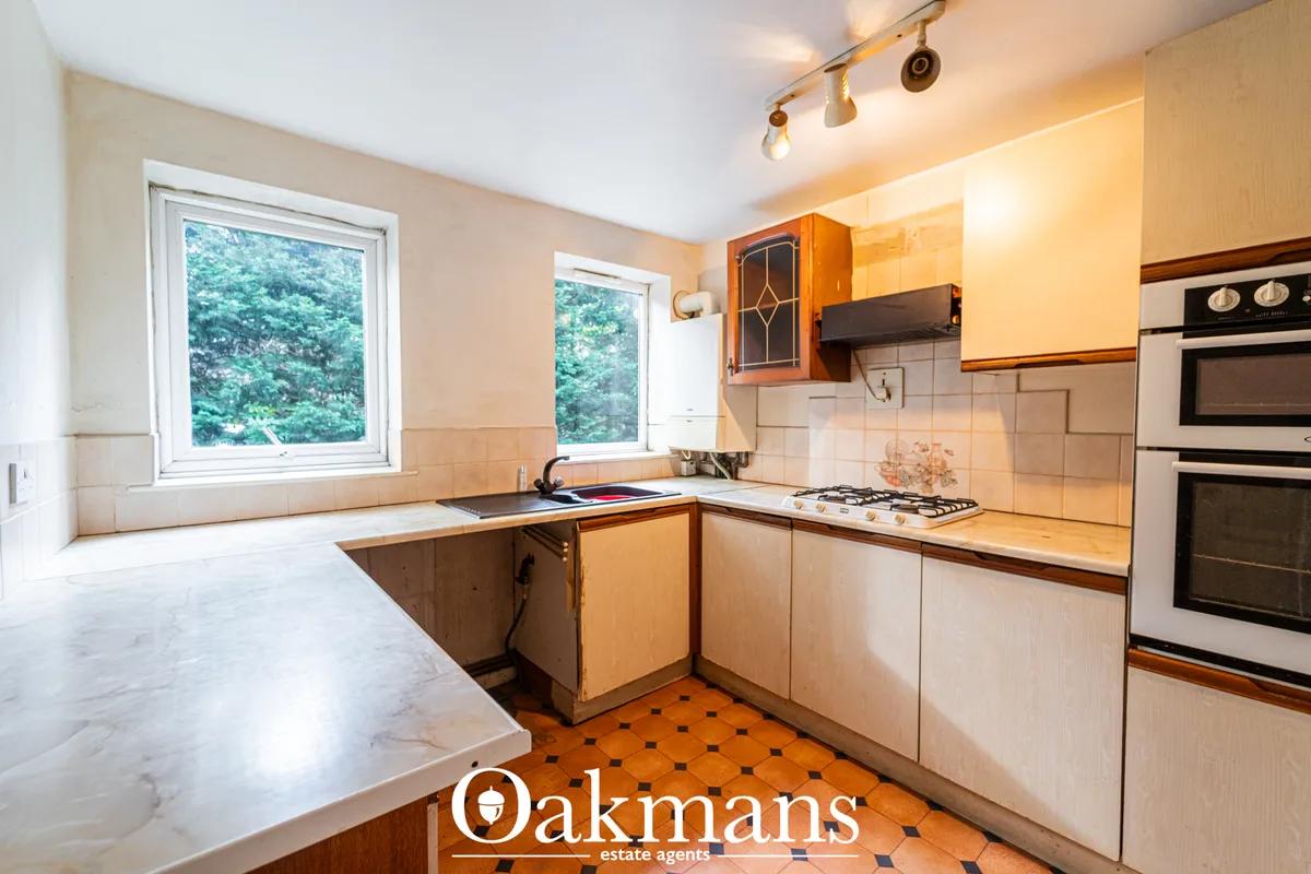 L-shaped kitchen with wooden cabinets, cream tile splashback, gas hob, integrated ovens, marble worktops and two windows