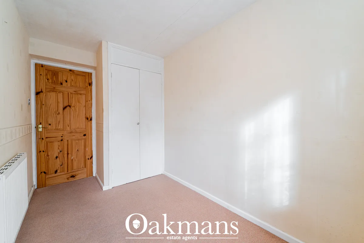 Bright hallway with cream walls, beige carpet, wooden pine door, white built-in wardrobe, radiator and natural sunlight 