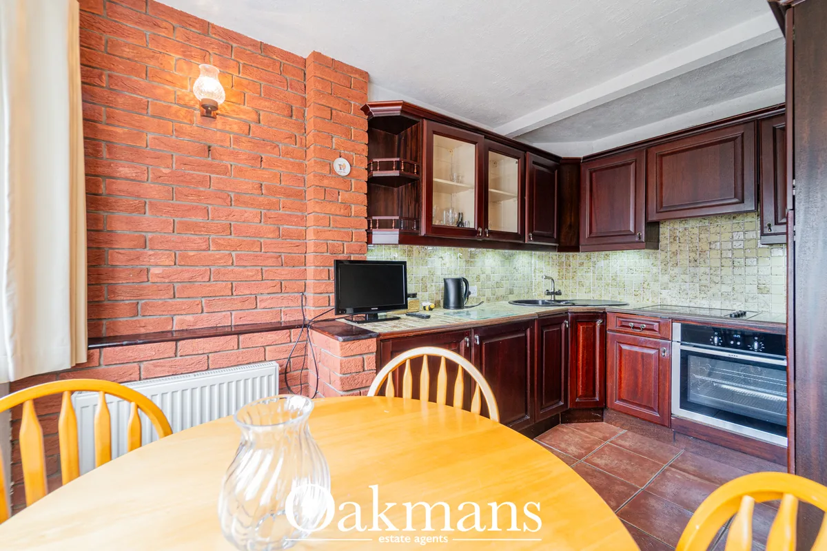 Modern kitchen with dark wood cabinetry, cream tile backsplash, built-in oven, and dining area with yellow chairs