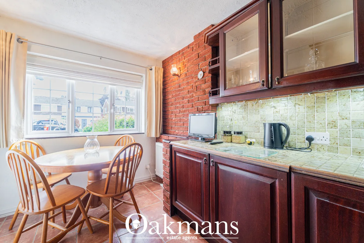 Kitchen with dark wood cabinetry, red brick feature wall, cream tile splashback, round dining table with wooden chairs a
