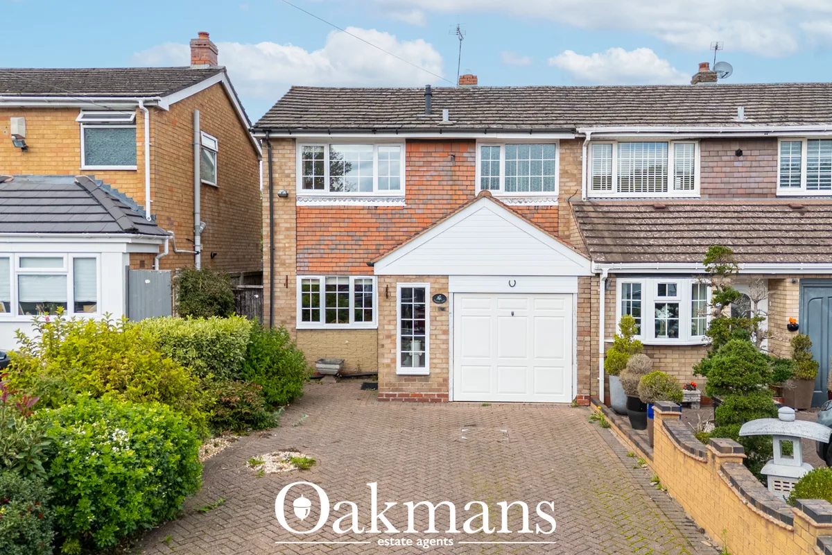 Brick-built semi-detached house with white garage door, driveway, manicured hedges and neighbouring properties