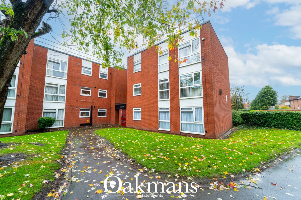 Red brick residential apartment building with manicured lawn, autumn foliage, and central entrance courtyard