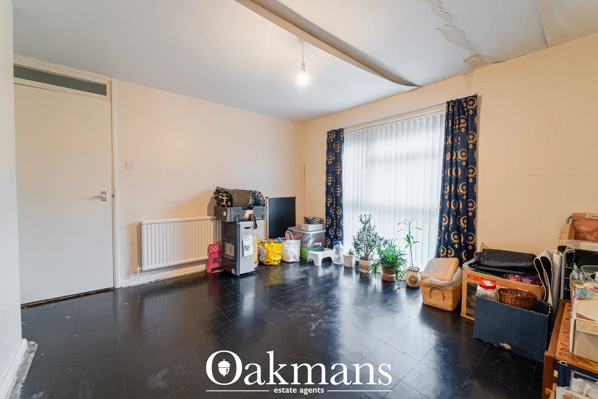 Spacious utility room with dark tiled flooring, cream walls, radiator, patio doors with patterned curtains, storage item