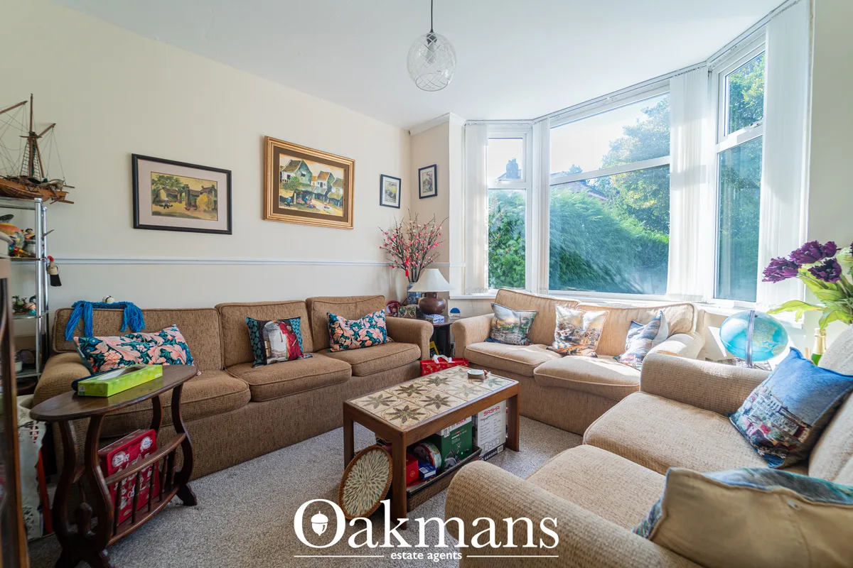 Spacious living room with beige upholstered seating, large bay windows overlooking garden, framed artwork, pendant light