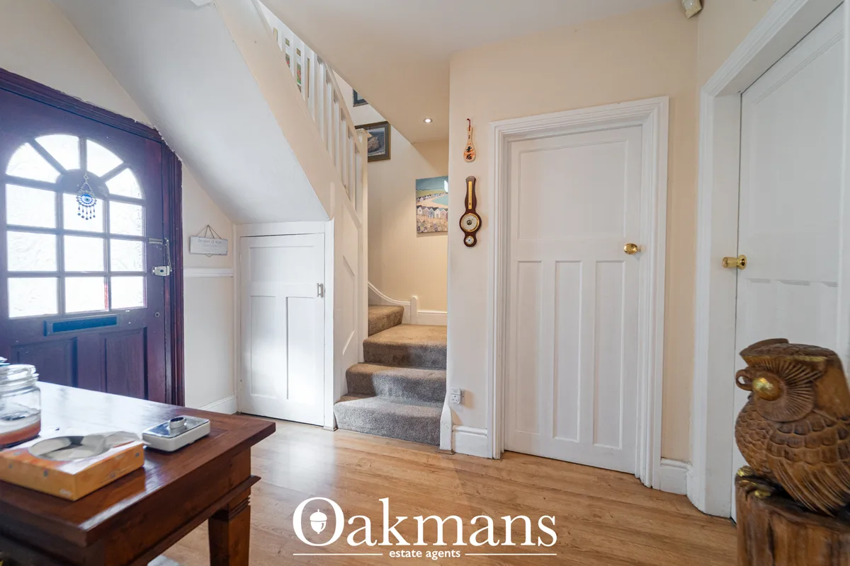 Bright entrance hallway with wooden flooring, cream walls, white doors, staircase with carpet runner, and purple-framed 