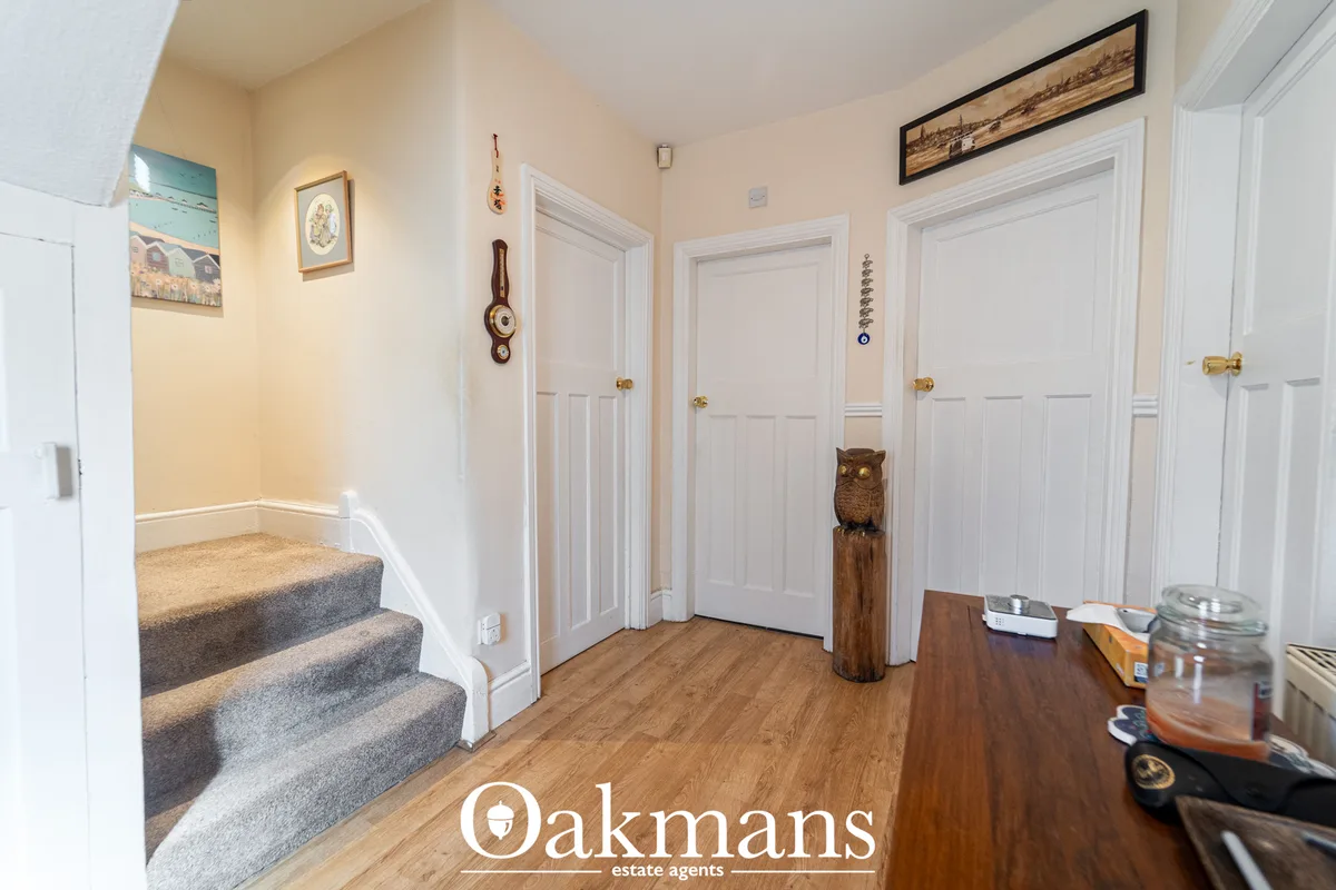 Bright entrance hallway with wooden flooring, multiple white panel doors with brass handles, carpeted staircase, cream w