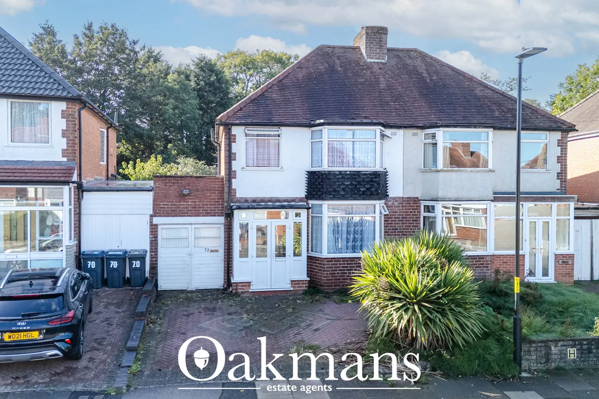Red-brick semi-detached house with white render, hipped roof, driveway with parked car, front garden with shrubs and str