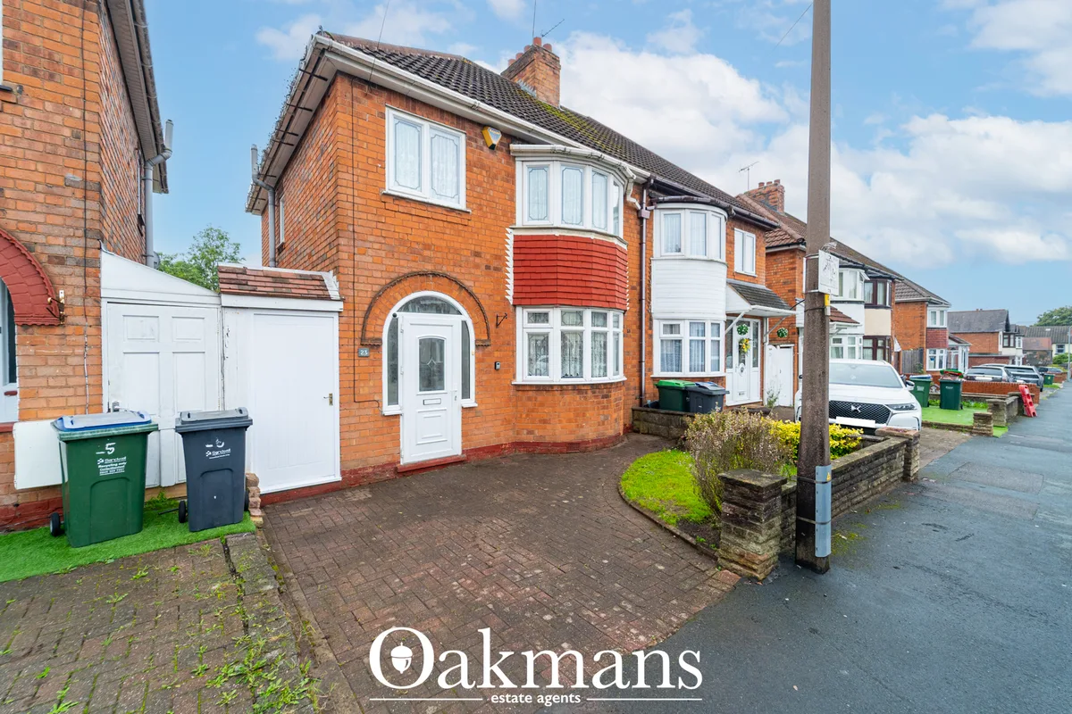 Red brick semi-detached house with white bay windows, arched entrance door, driveway, and garage on residential street