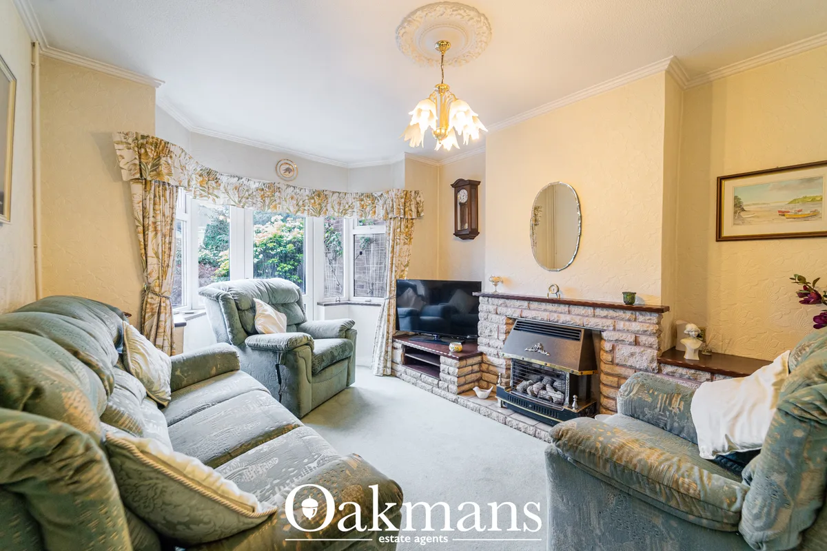 Spacious living room with cream walls, green upholstered furniture, fireplace with stone surround, TV, pendant chandelie