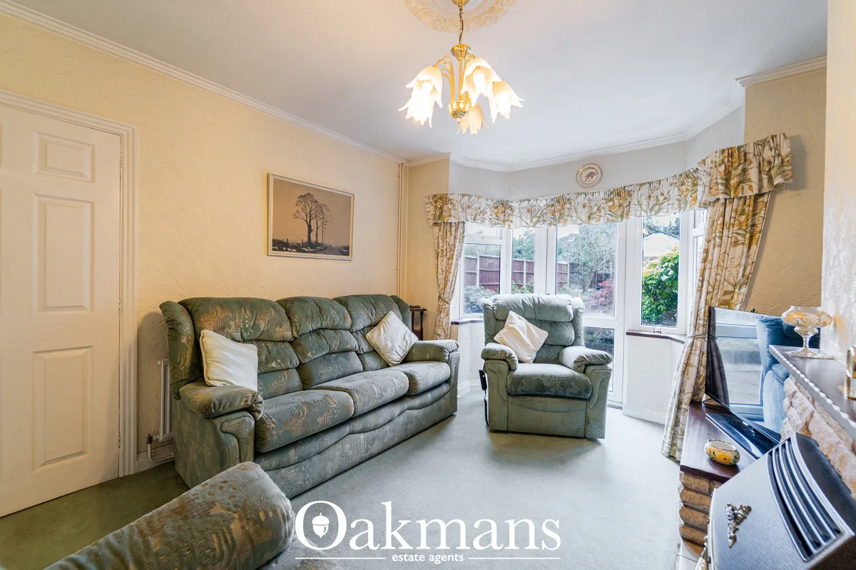 Spacious living room with green patterned sofa and armchair, patio doors overlooking garden, ornate ceiling rose and pen