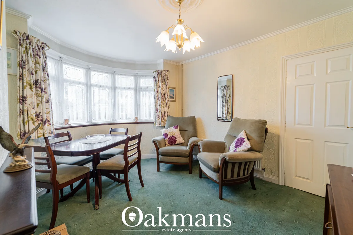 Elegant living room with bay windows, cream walls, beige armchairs with purple cushions, dining table, patterned curtain