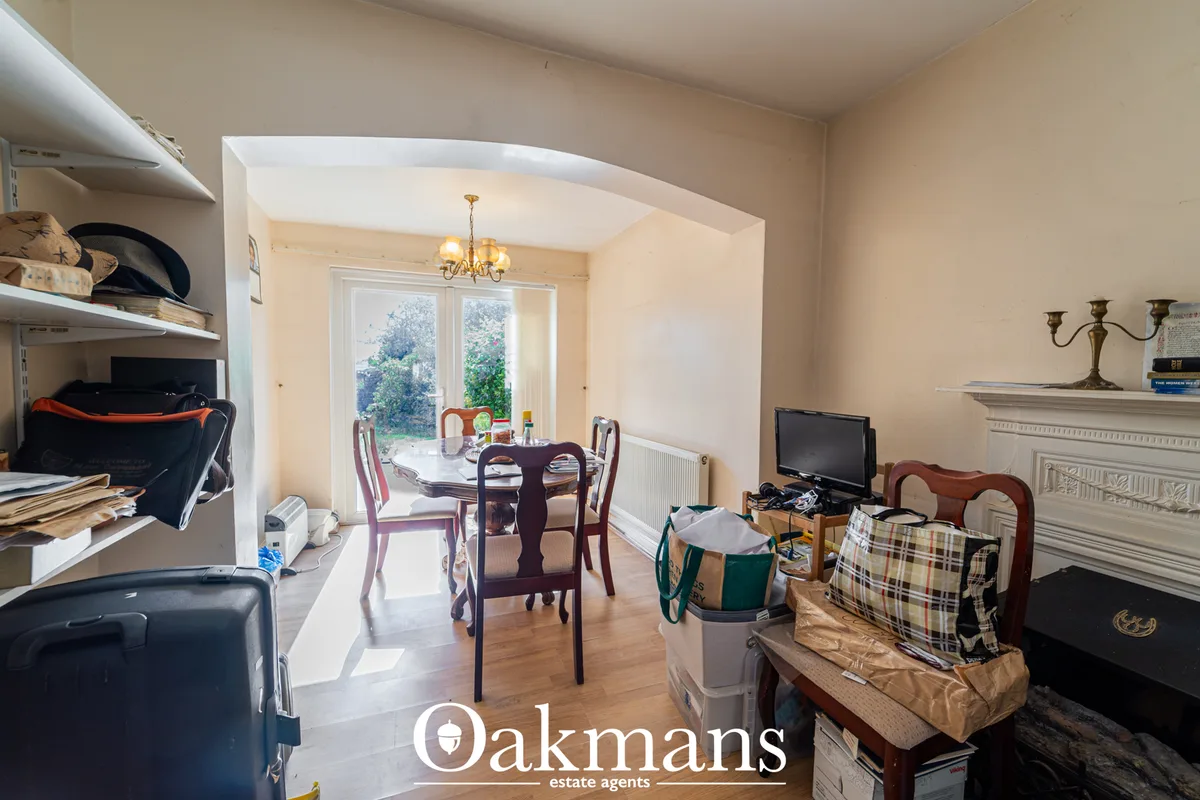 Open-plan living and dining area with wooden flooring, cream walls, fireplace, TV, dining table with chairs, archway to 