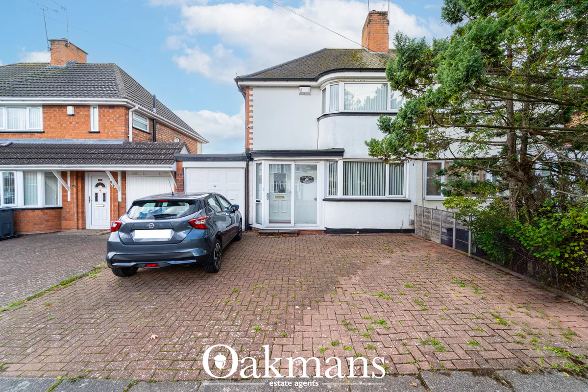 Two-storey suburban semi-detached houses with brick and render facades, parked car on herringbone driveway, ivy-covered 