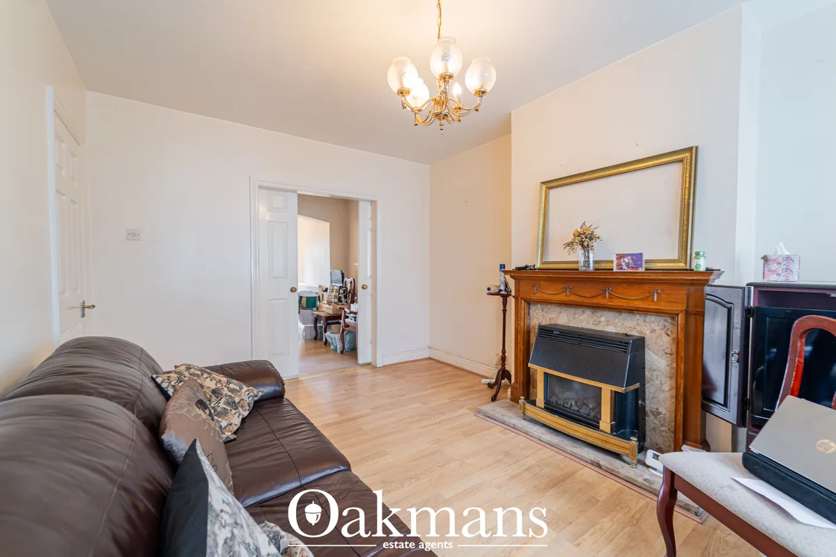 Spacious living room with brown leather sofa, wooden fireplace with mirror above, wooden flooring, pendant chandelier an