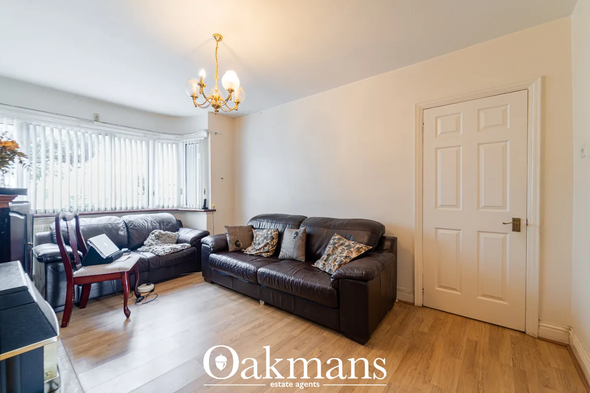 Spacious living room with dark leather sofas, cream walls, wooden flooring, gold chandelier, vertical blinds and cream p