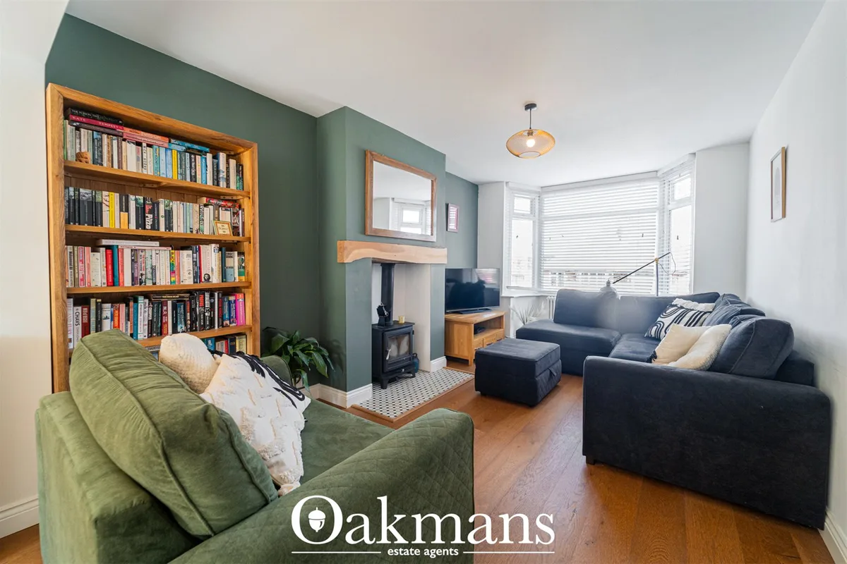 Spacious living room with green accent wall, wooden bookshelf, dark sofas, wood-burning stove, large bay window with shu