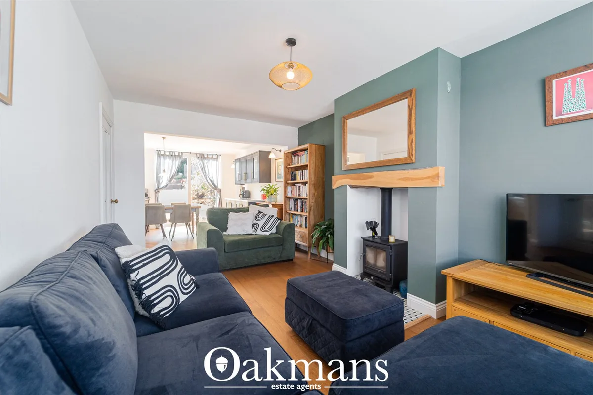 Open-plan living room with blue-grey walls, navy sofas, wooden TV unit, wood-burning stove with mirror above, bookshelf 