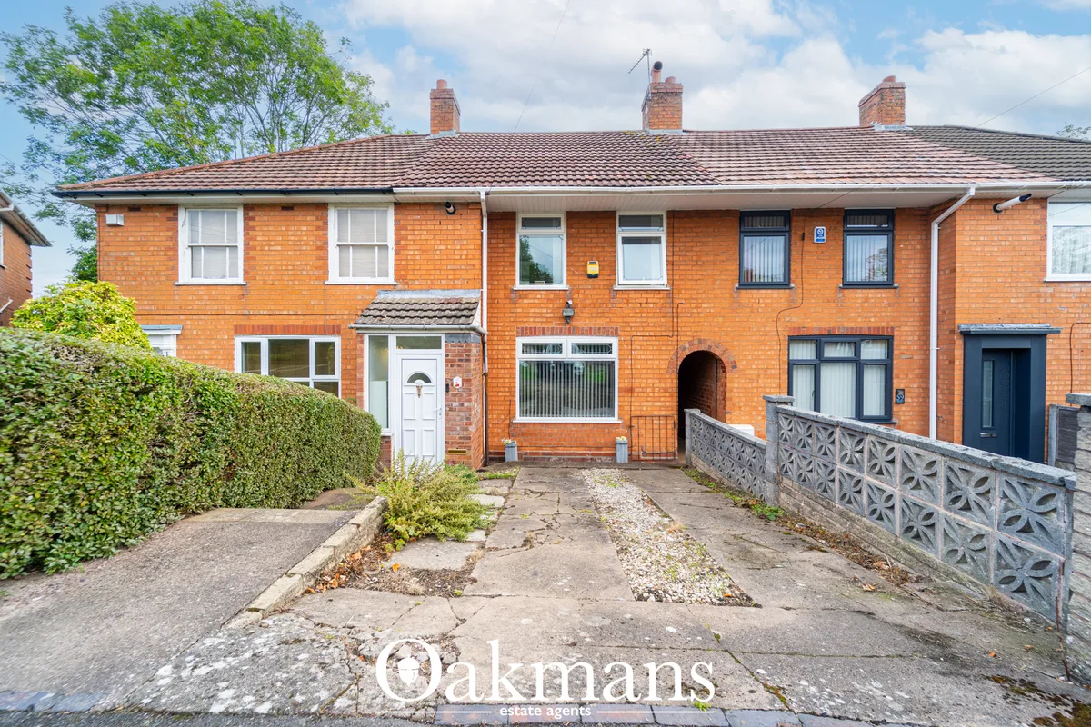 Red brick terraced house with tiled roof, bay windows, white door, hedged front garden and paved pathway