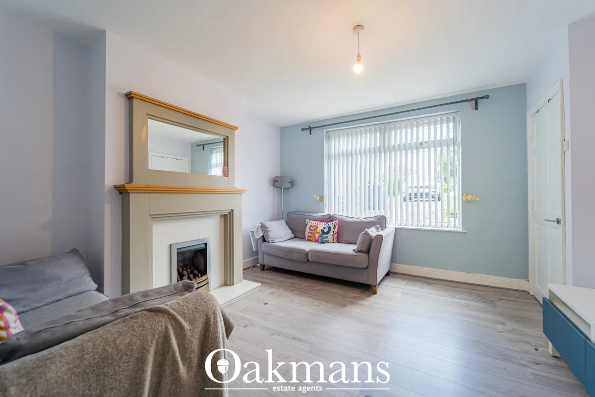 Bright living room with fireplace, grey sofa, vertical blinds on large window, light wood flooring and blue accent wall