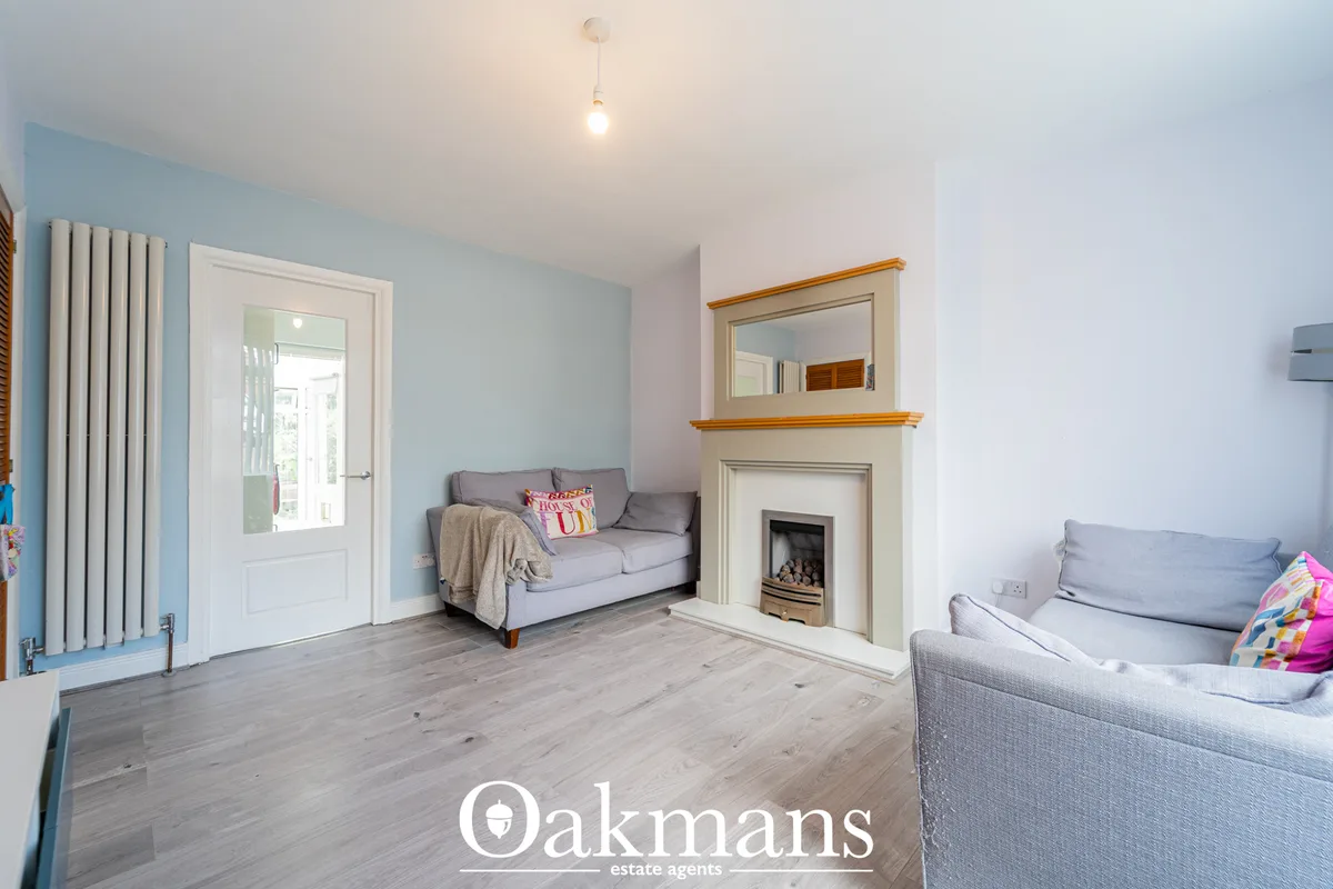 Bright living room with light blue walls, two grey sofas, fireplace with wooden mantelpiece, wooden flooring, and white 