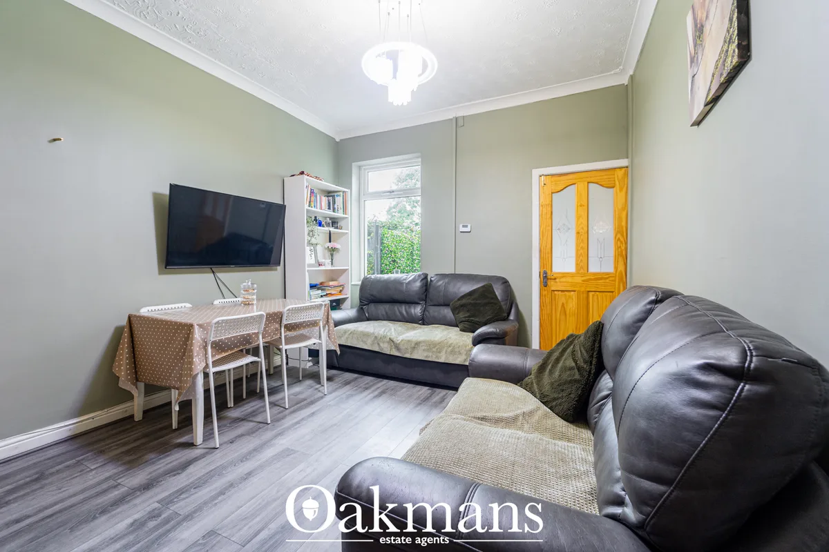 Spacious living room with pale green walls, black leather sofas, wall-mounted TV, wooden double doors, large window, din