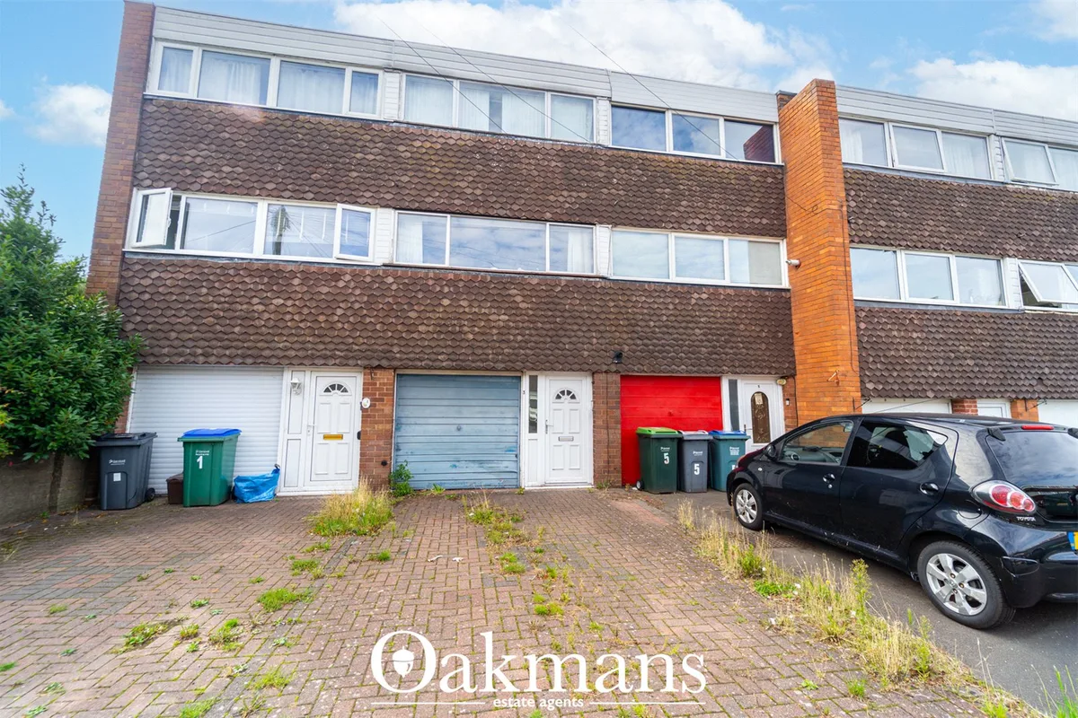 Front façade of brick terraced house with three garage doors, rendered roof sections, ground-floor windows, and parked c