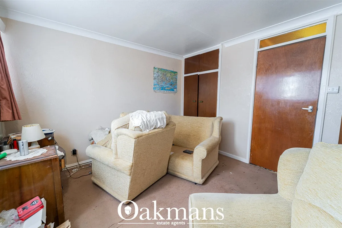 Living room with two cream upholstered armchairs, wooden furniture, brown wooden doors, cream walls and carpet flooring